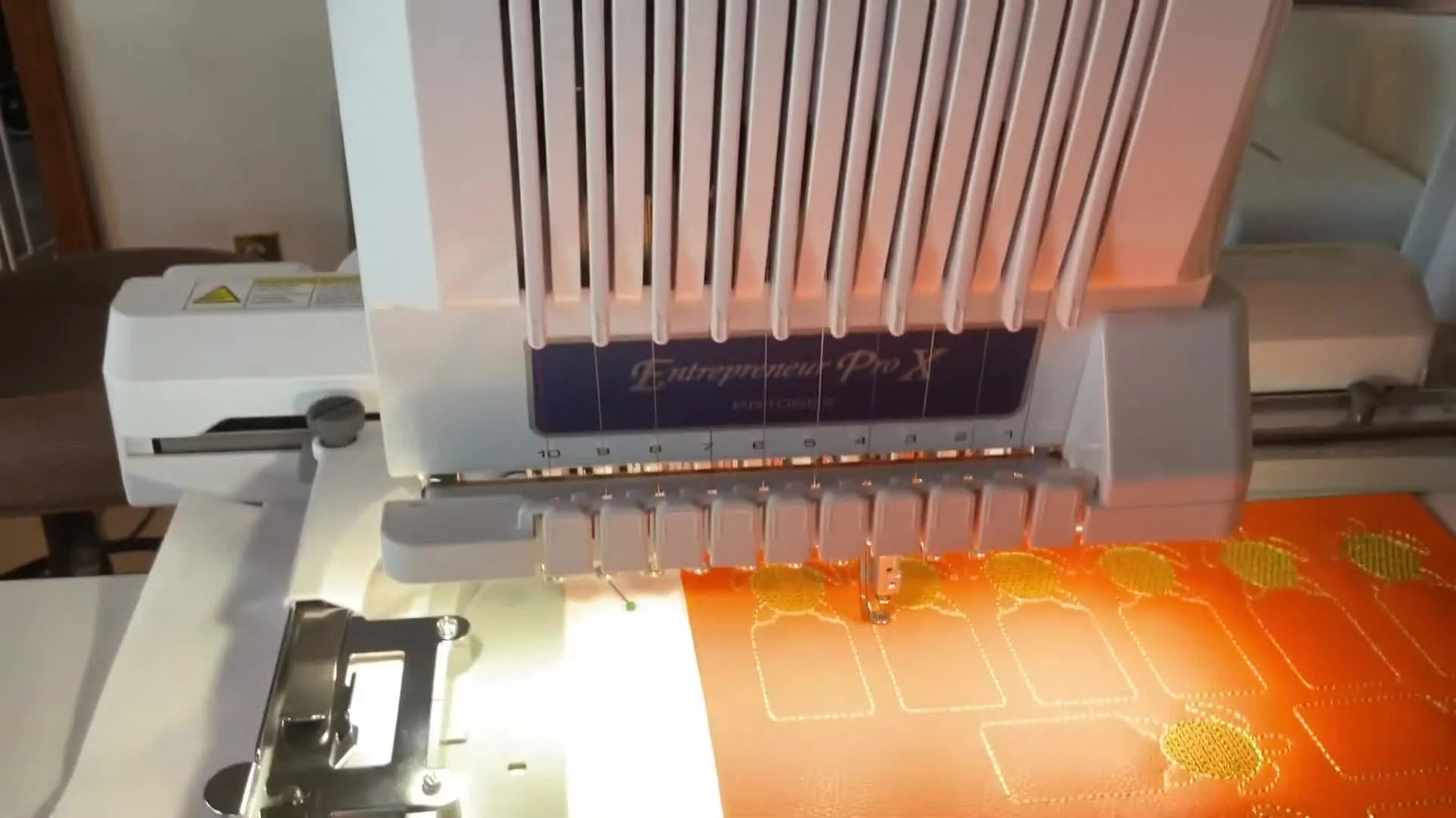 A Brother PR1050X stitches the final gold outline on a full hoop of faux leather bookmarks while pins hold the backing fabric in place.