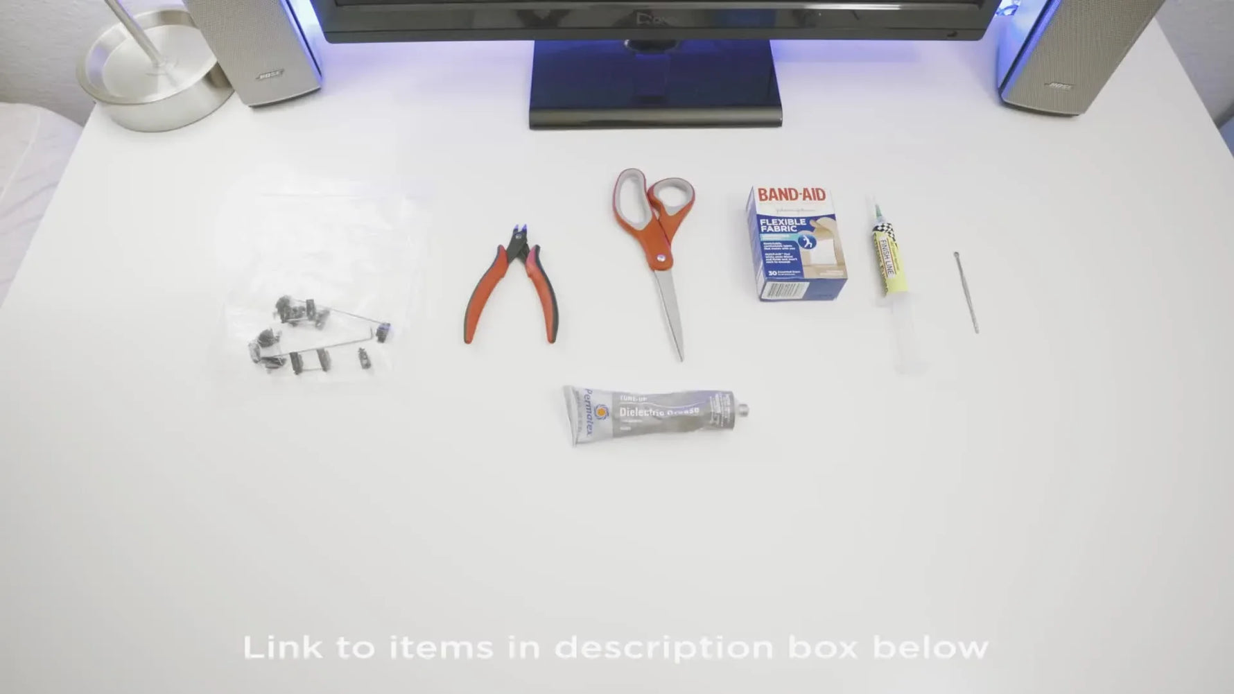 A white desk displaying all the tools and materials needed for stabilizer modding, including stabilizers, wire cutters, scissors, band-aids, dielectric grease, Teflon grease, and an earwax picker.