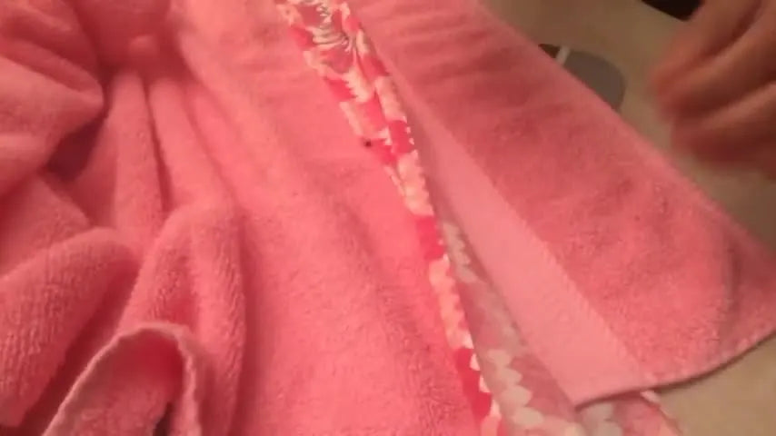 Hands guiding the pink towel with the pinned fabric strip under the presser foot of a sewing machine.