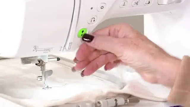 The Brother Innov-is NQ3600D stitches a heart outline on hooped white fabric while the green start button indicates it’s ready to run.