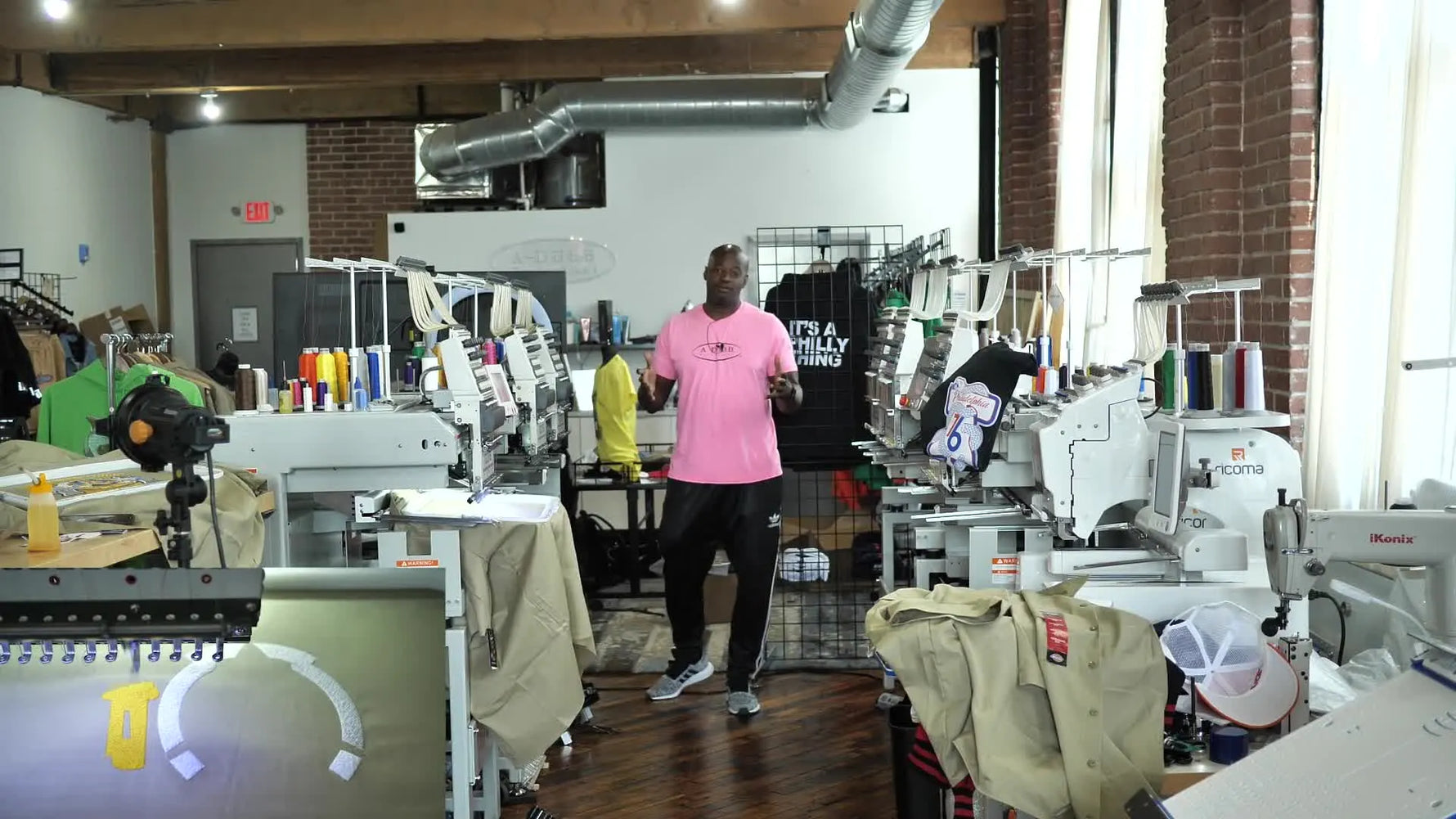 The shop owner stands in front of multiple commercial embroidery heads, showing what scaling looks like in a real production space.