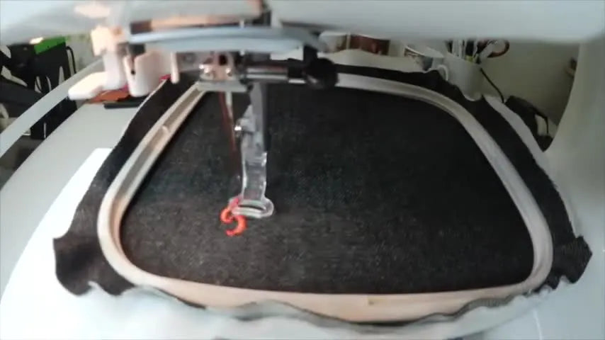 Close-up action shot of the Janome 350E stitching a red letter on dark denim while the hoop moves smoothly under the needle.