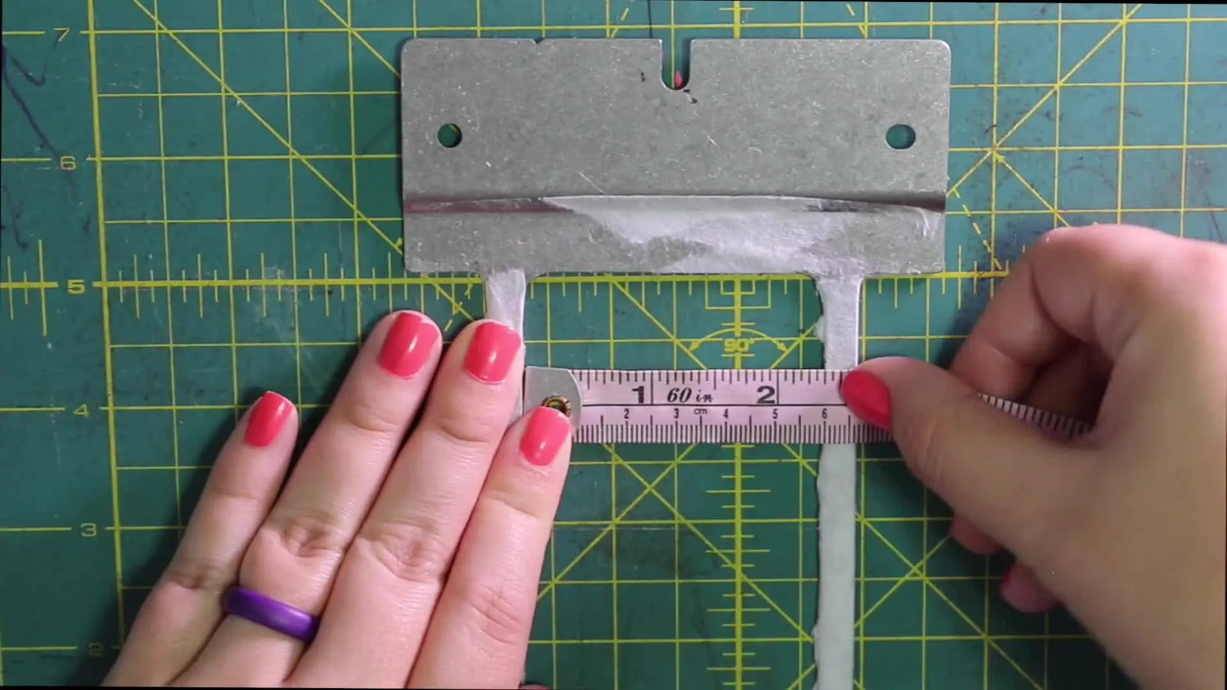 A pink flexible measuring tape spans the inside width of a metal Fast Frame, showing a 60mm reading before applying a safety buffer.