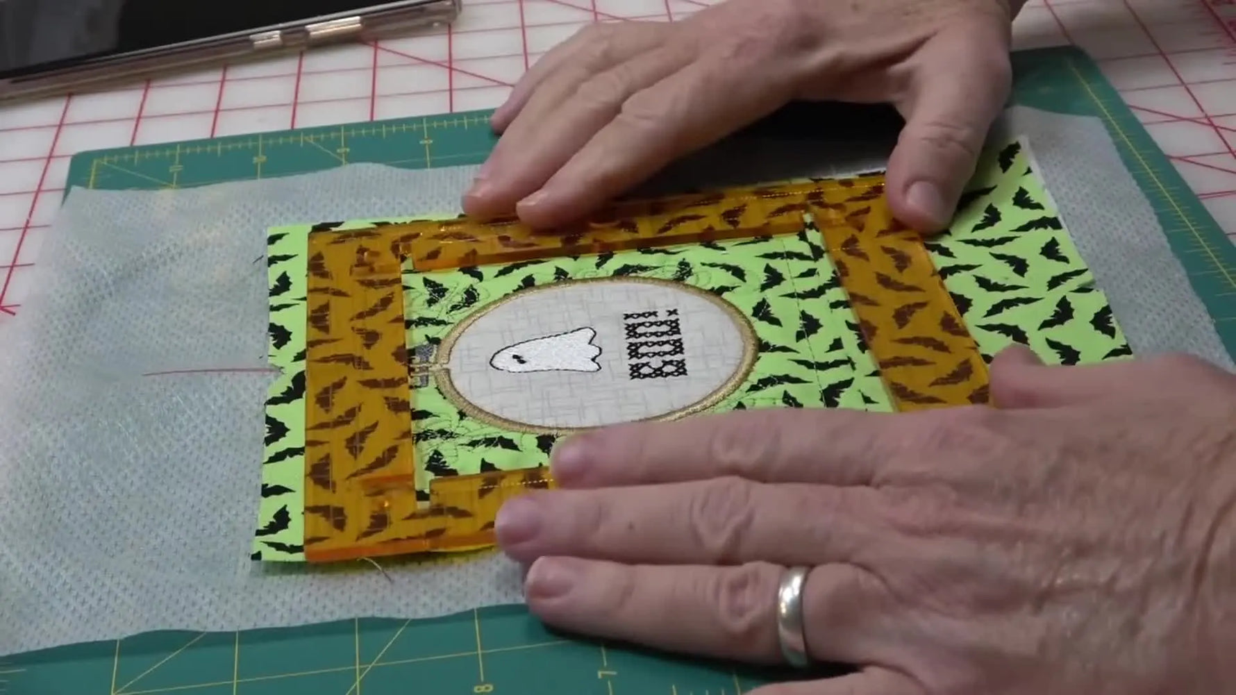 A rotary cutter trims the finished Boo Hoop block to a precise square using an Orange Pop Ruler on a cutting mat.