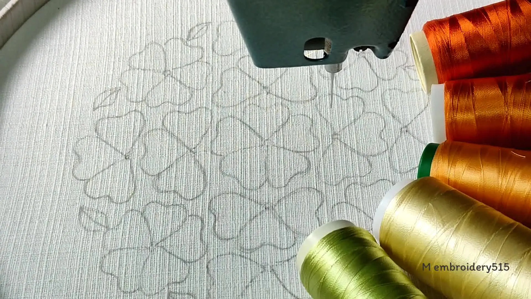 An overhead shot of an embroidery hoop with a fabric, showing a pre-drawn floral pattern and various spools of thread.