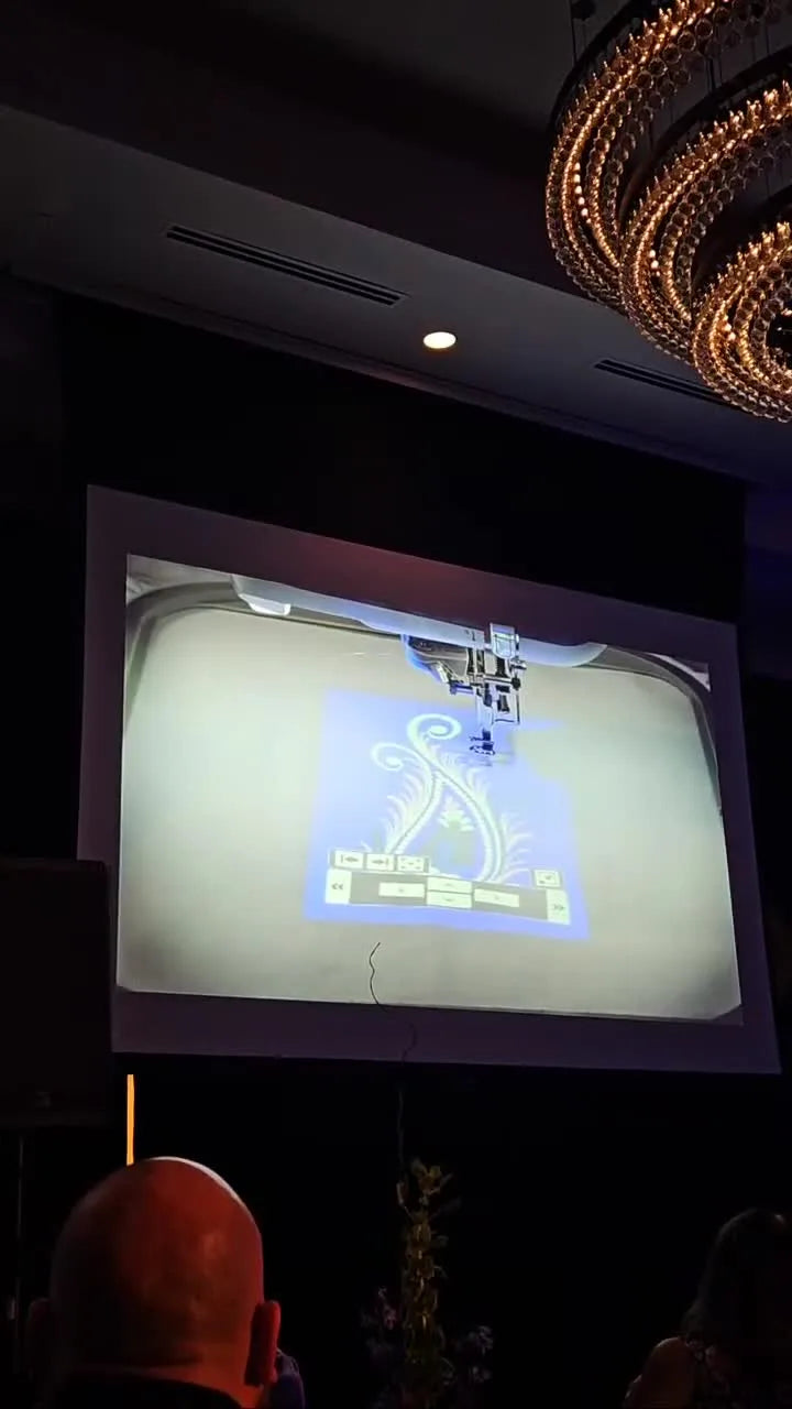 A bright blue paisley design is projected onto hooped fabric, showing how the Brother Aveneer EV1’s 8" × 5" projection field helps with precise placement.