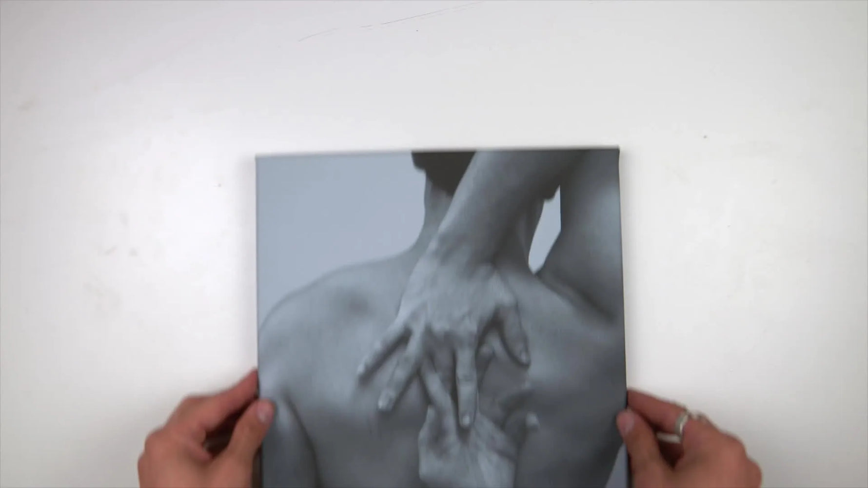 A close-up of hands holding an embroidered photograph of a man's back, featuring intricate floral designs stitched onto the image.