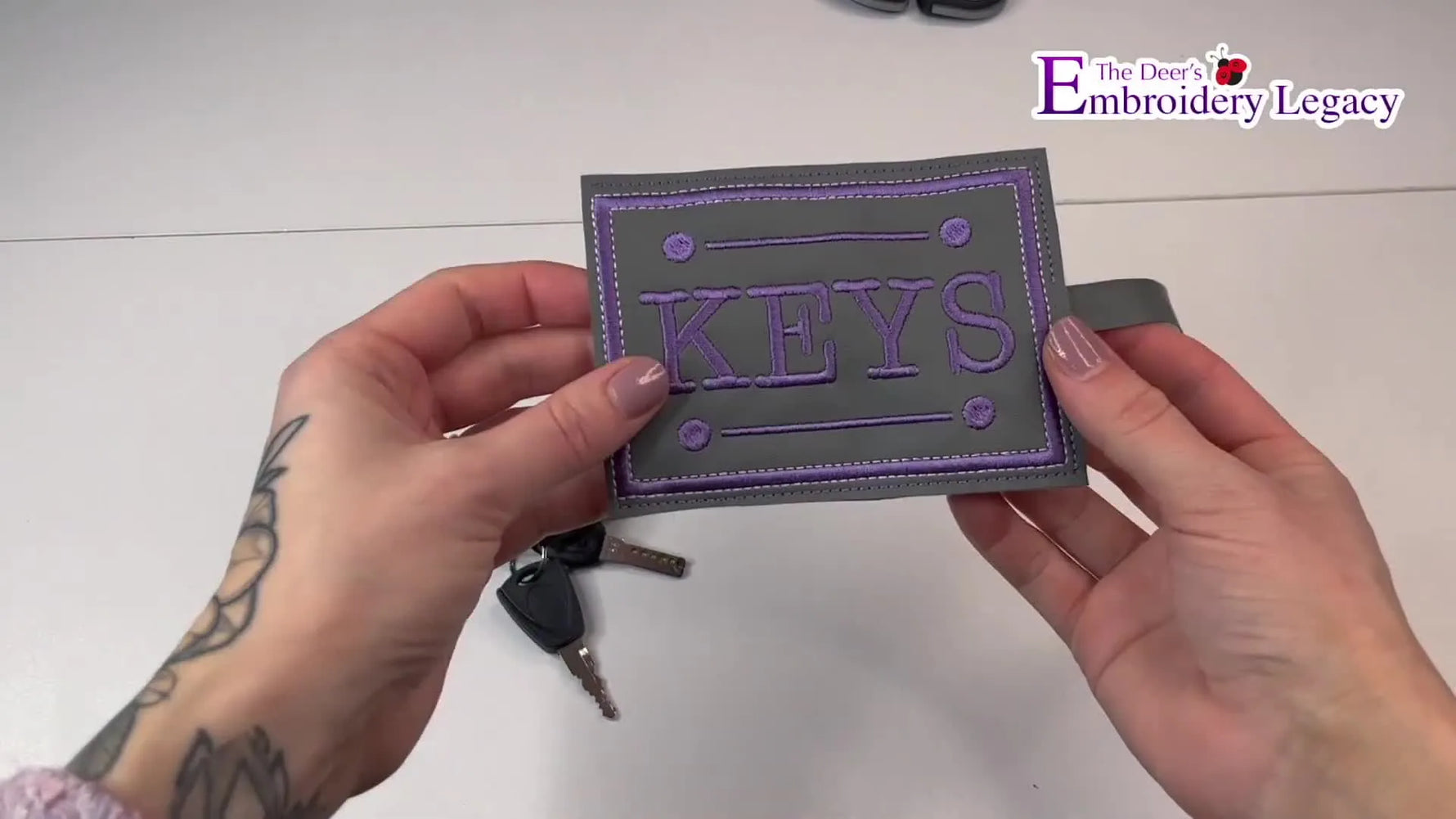 A close-up of the finished in-the-hoop key holder with keys attached, showing the clean stitched border and snap-strap assembly.