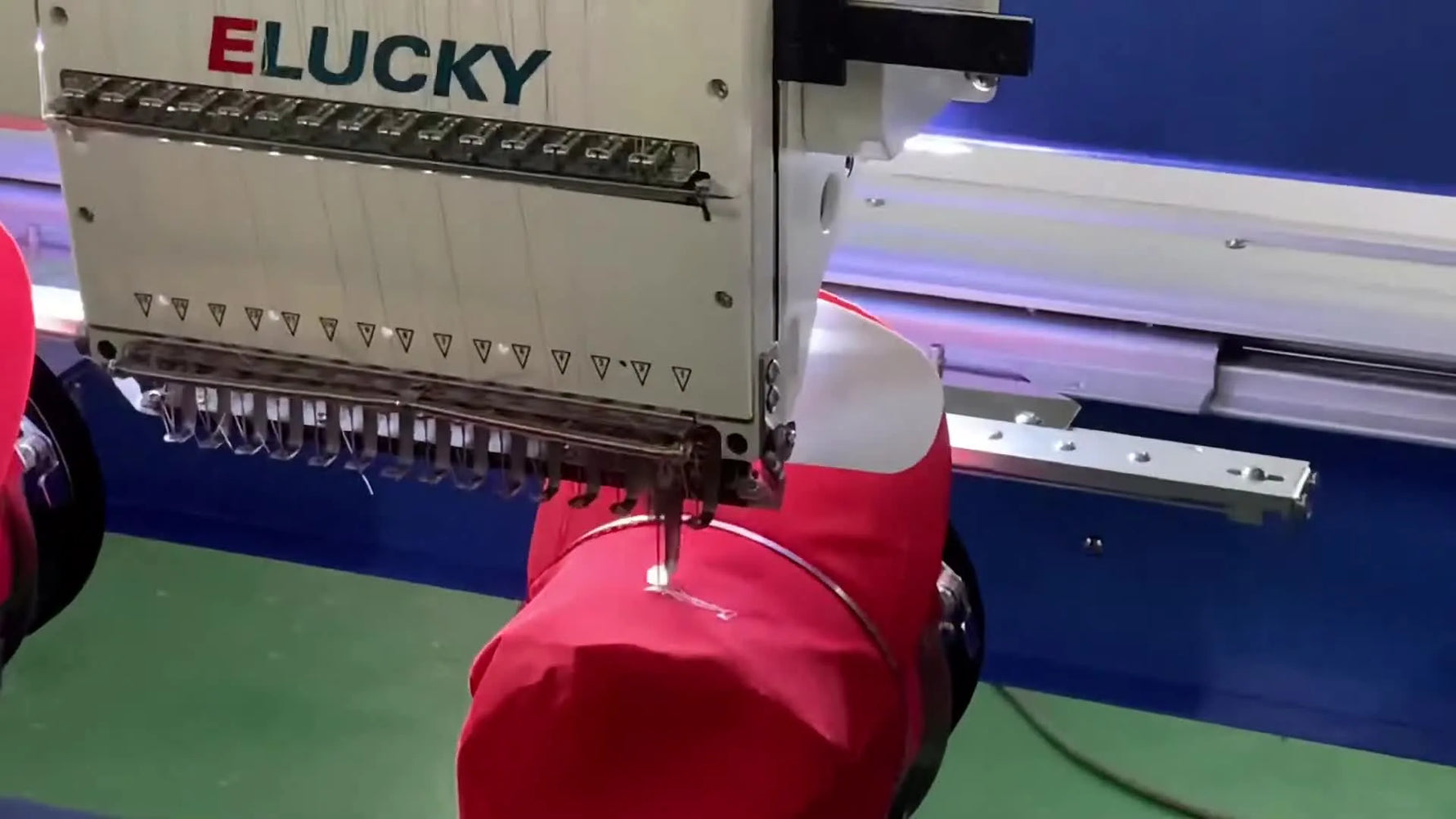 An extreme close-up of the needle stitching a white logo onto a red cap during an ELUCKY dual-head embroidery run.