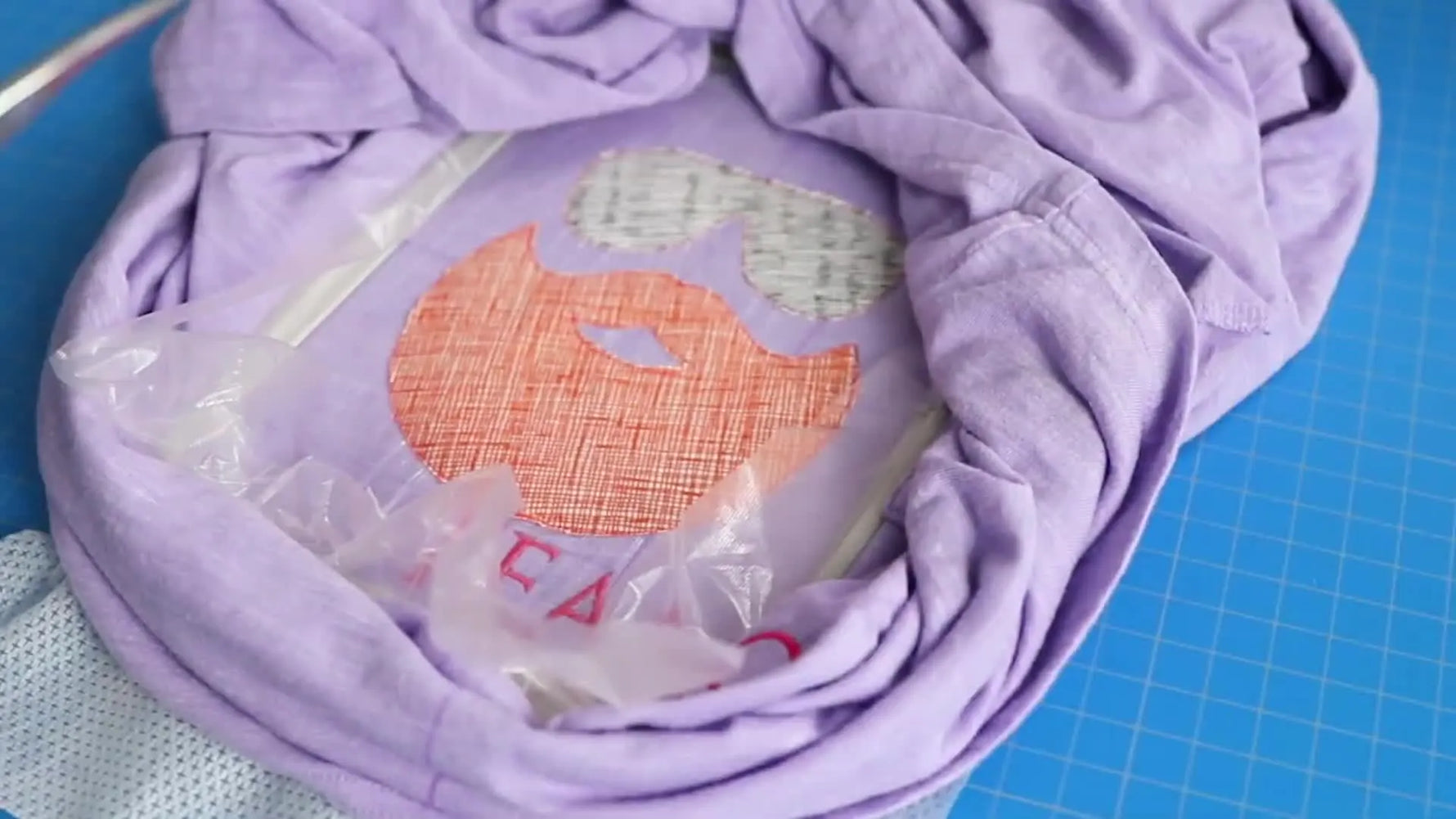 Close-up of a Brother PE800 stitching a dense satin border around a raw-edge beard-and-sunglasses appliqué on a purple T-shirt.