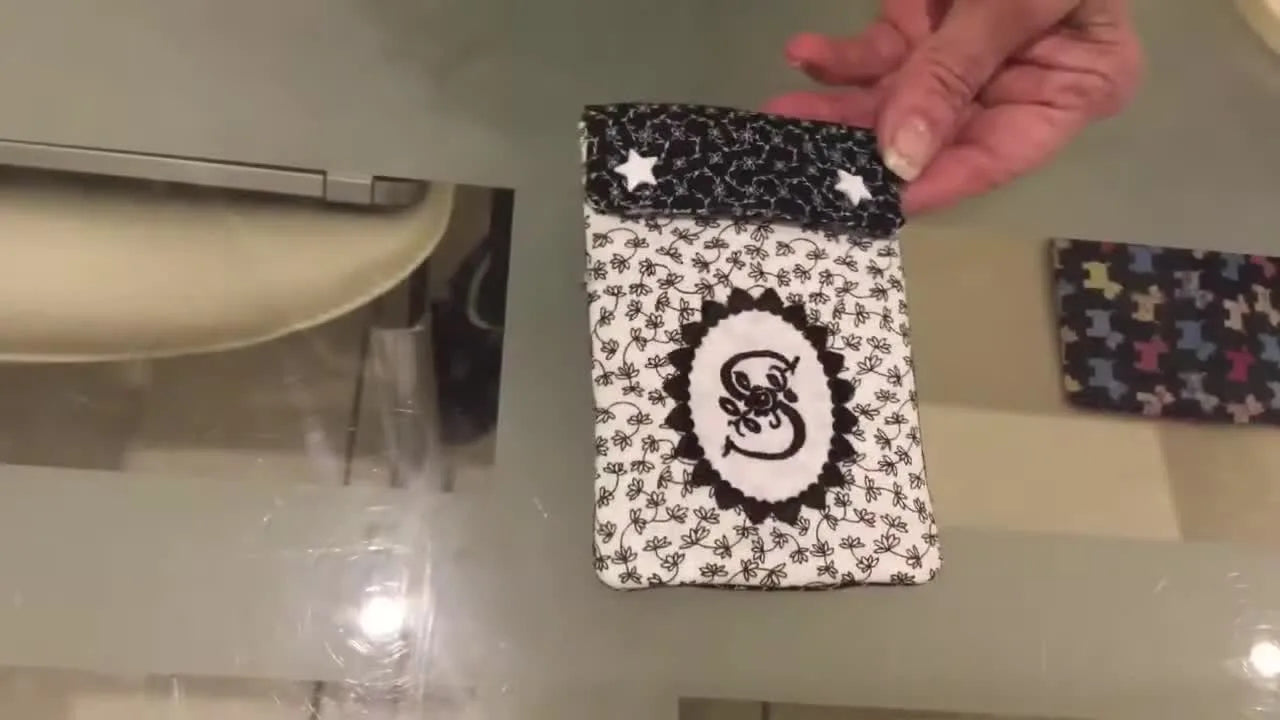 A finished fully lined in-the-hoop phone case/purse with a monogram and snap studs, shown close-up after turning and pressing.