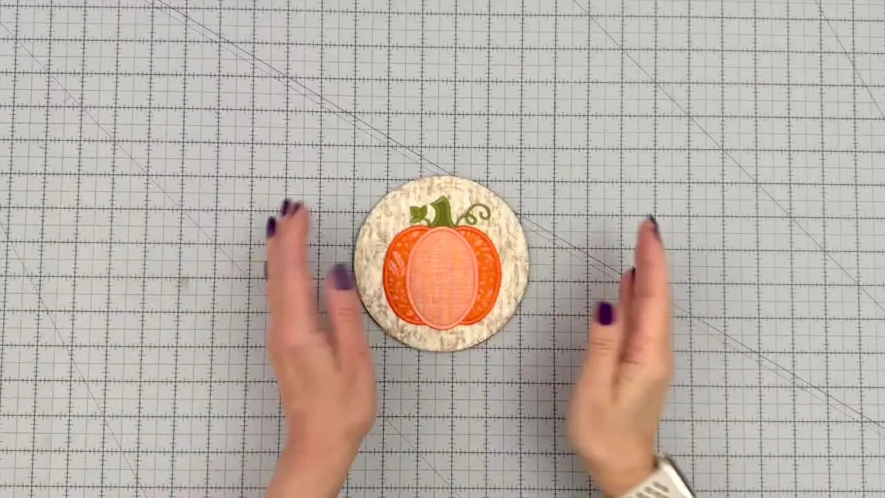 A finished pumpkin coaster is shown alongside a larger pumpkin hot pad on a cutting mat, highlighting the matching ITH construction in two sizes.