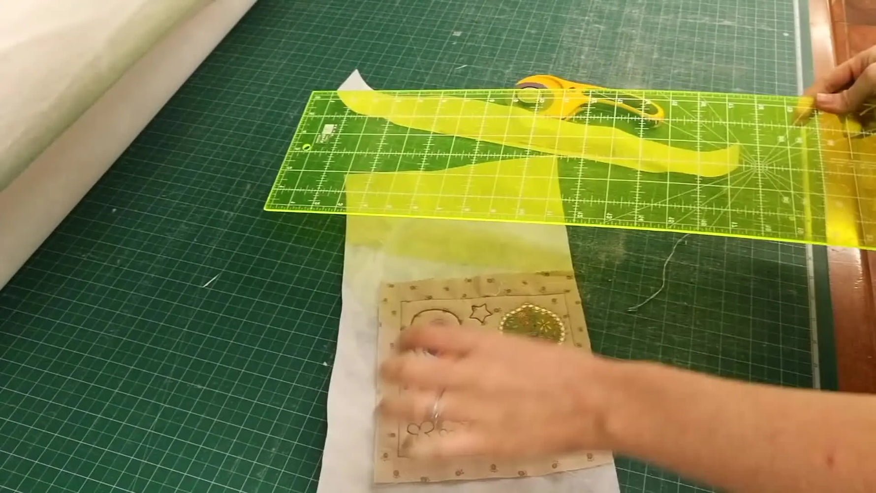 A finished, trimmed ITH quilt block is held up close, showing a bird appliqué with cross-hatch quilting and clean satin borders.