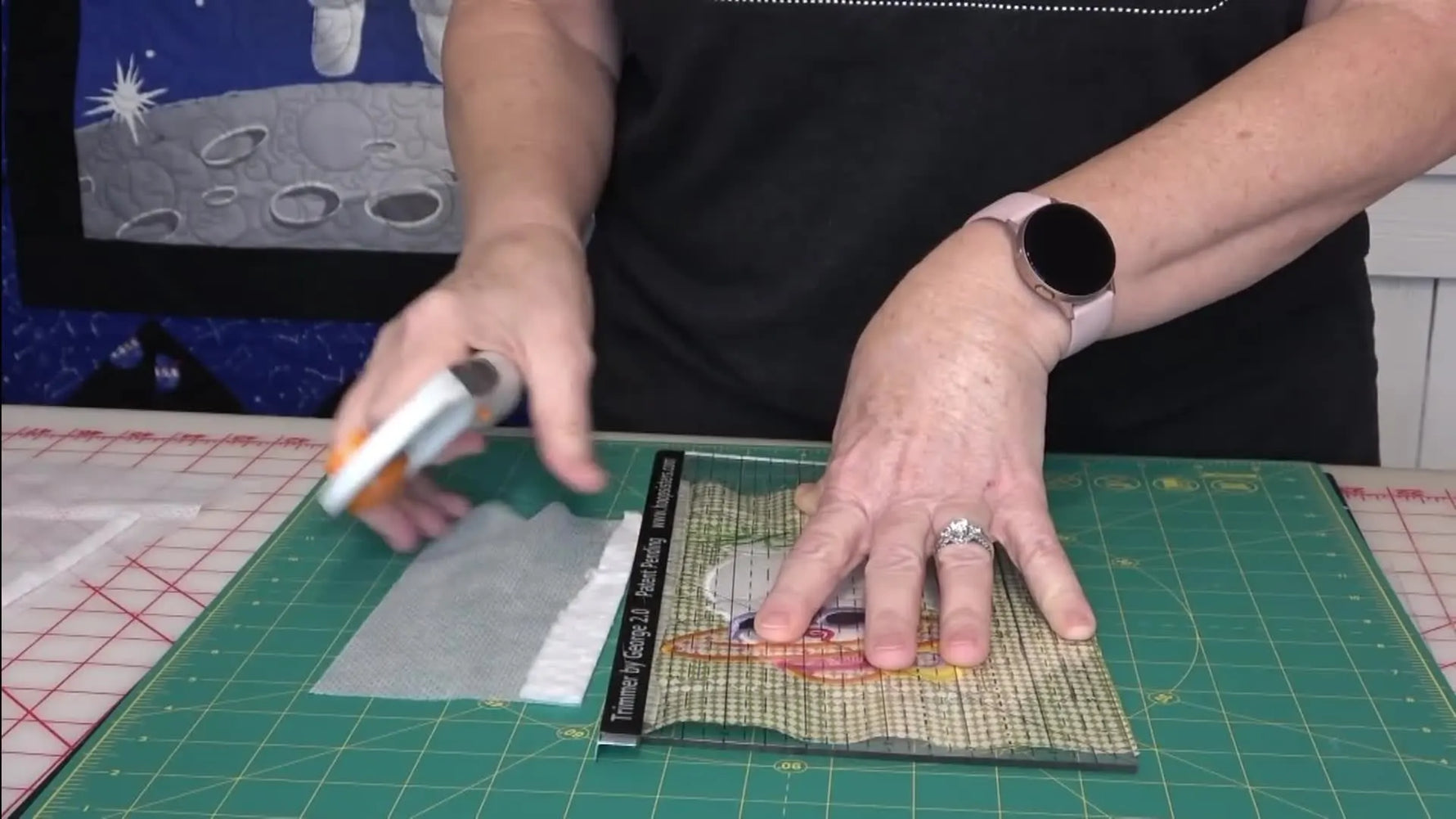 Hands hold the Trimmer by George 2.0 ruler, highlighting the metal lip used to trim batting cleanly without cutting into the stitched seam line.