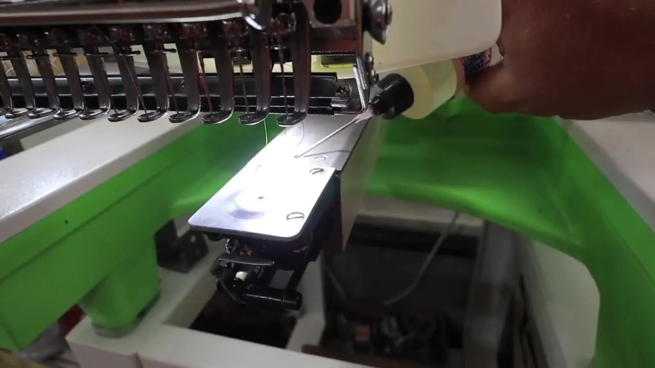 Close-up of oil being applied to the rotary hook assembly under the needle plate on a Smartstitch 15-needle embroidery machine.