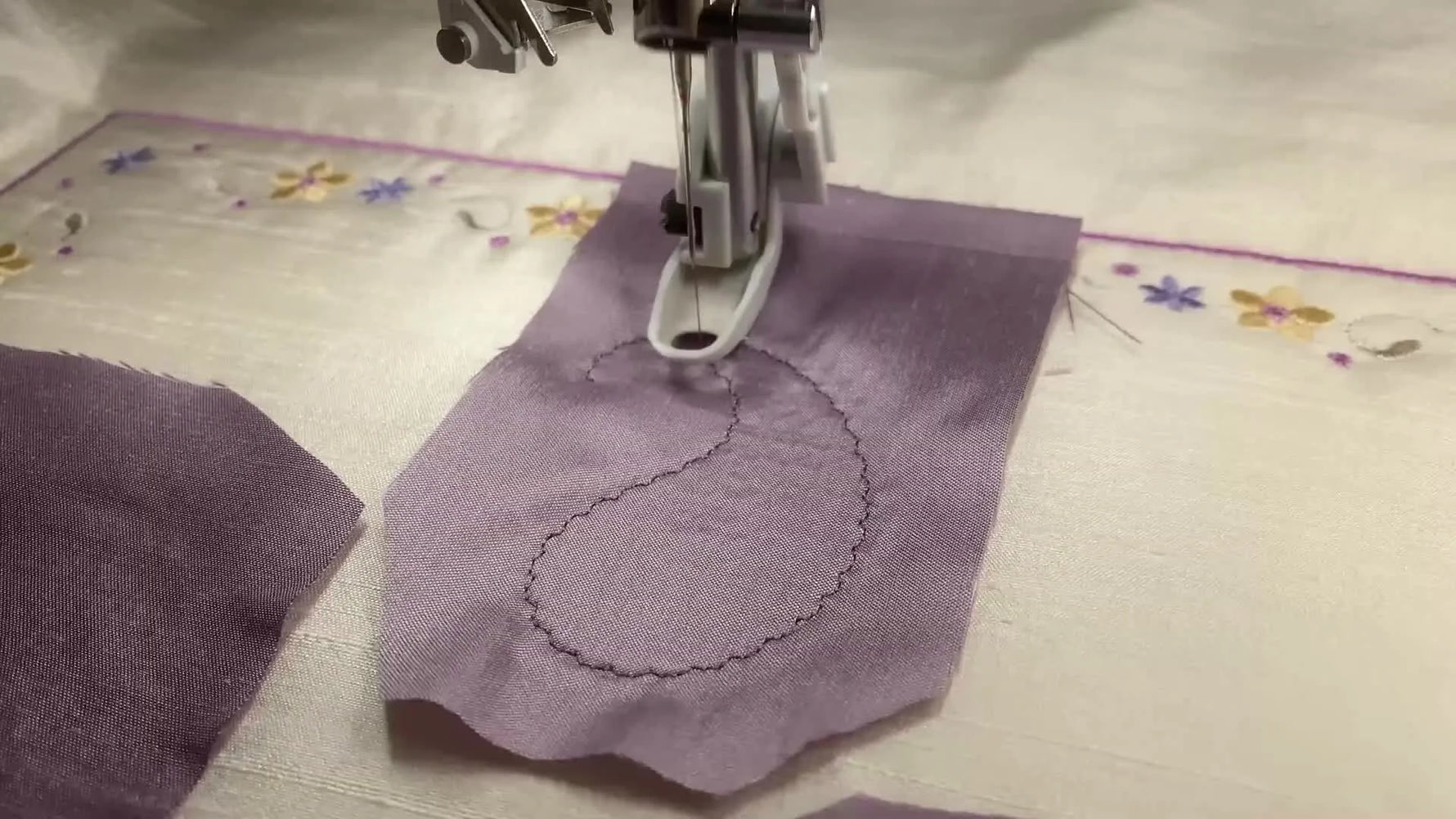 Extreme close-up of a decorative satin-style edge stitch forming a crisp border around a paisley applique on silk dupioni.