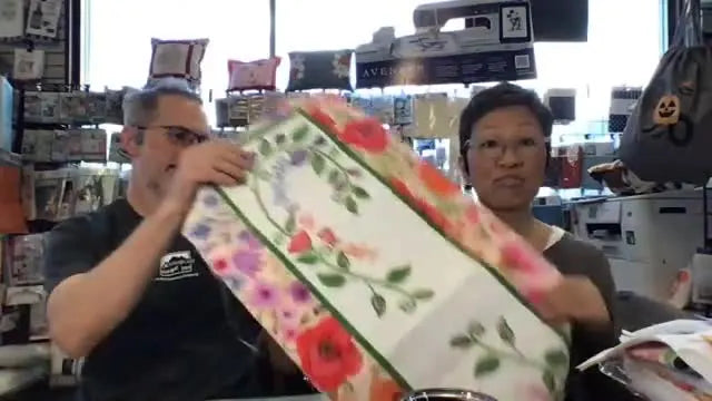 A fully stitched floral table runner is held up for a clear look at the embroidery detail and overall finish.