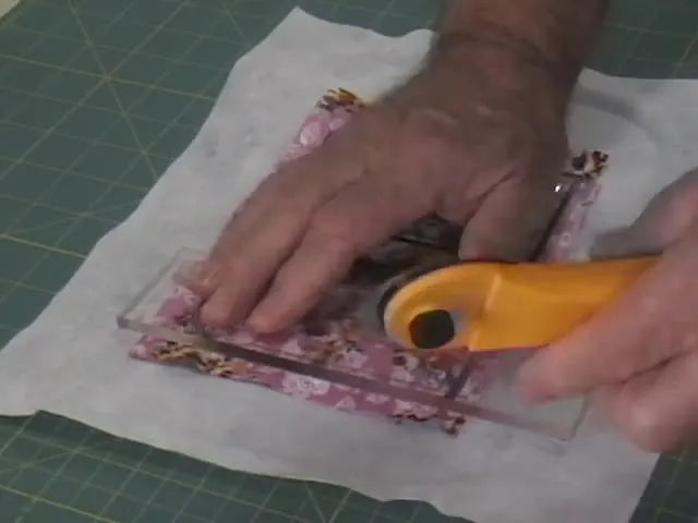 A close-up of trimming the stitched luggage tag cleanly with a rotary cutter guided by a clear ruler for a crisp, professional edge.