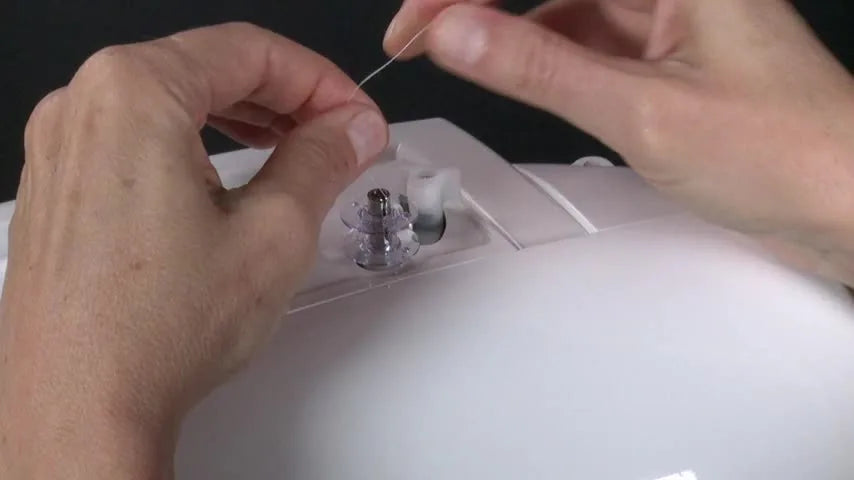 A close-up shows the Singer Futura bobbin winder lever being pushed to engage winding—one of the most common make-or-break moments for clean embroidery tension.