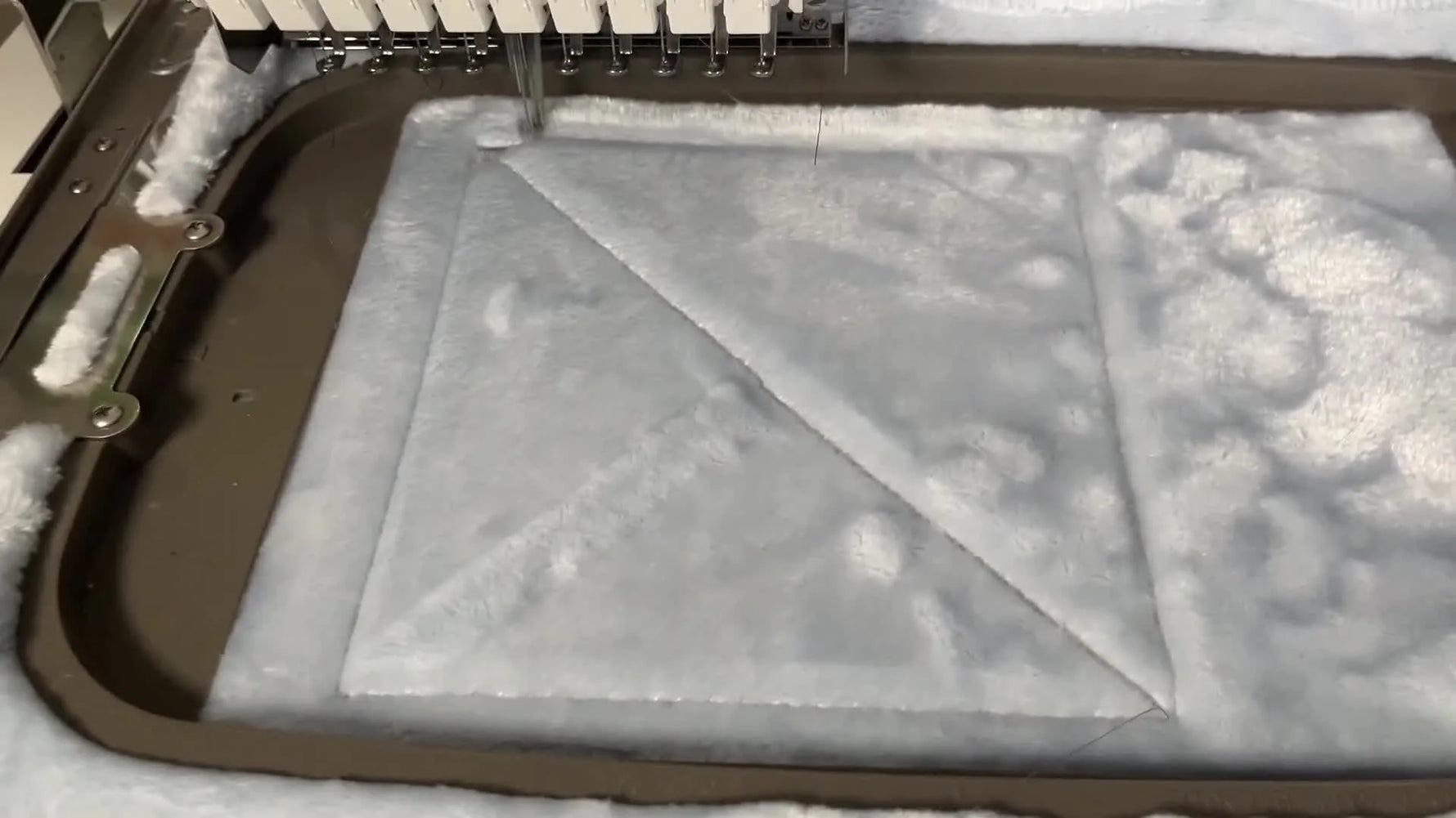 Close-up of the needle stitching the knockdown layer, showing the flattened base area contrasted against the surrounding plush pile.