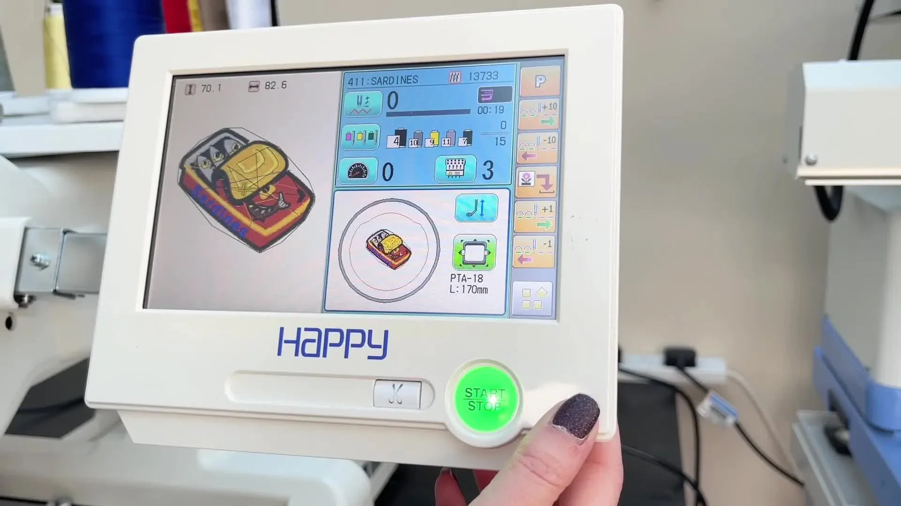 A close-up of a Happy Japan multi-needle machine stitching the final red-and-yellow sardine tin patch on white felt inside a tubular hoop.
