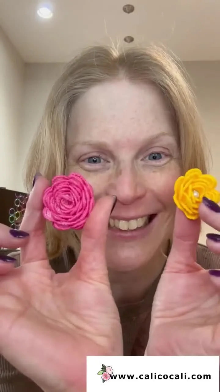 A close-up of two finished in-the-hoop lace rolled flowers (pink and yellow) held up to show their texture and shape.
