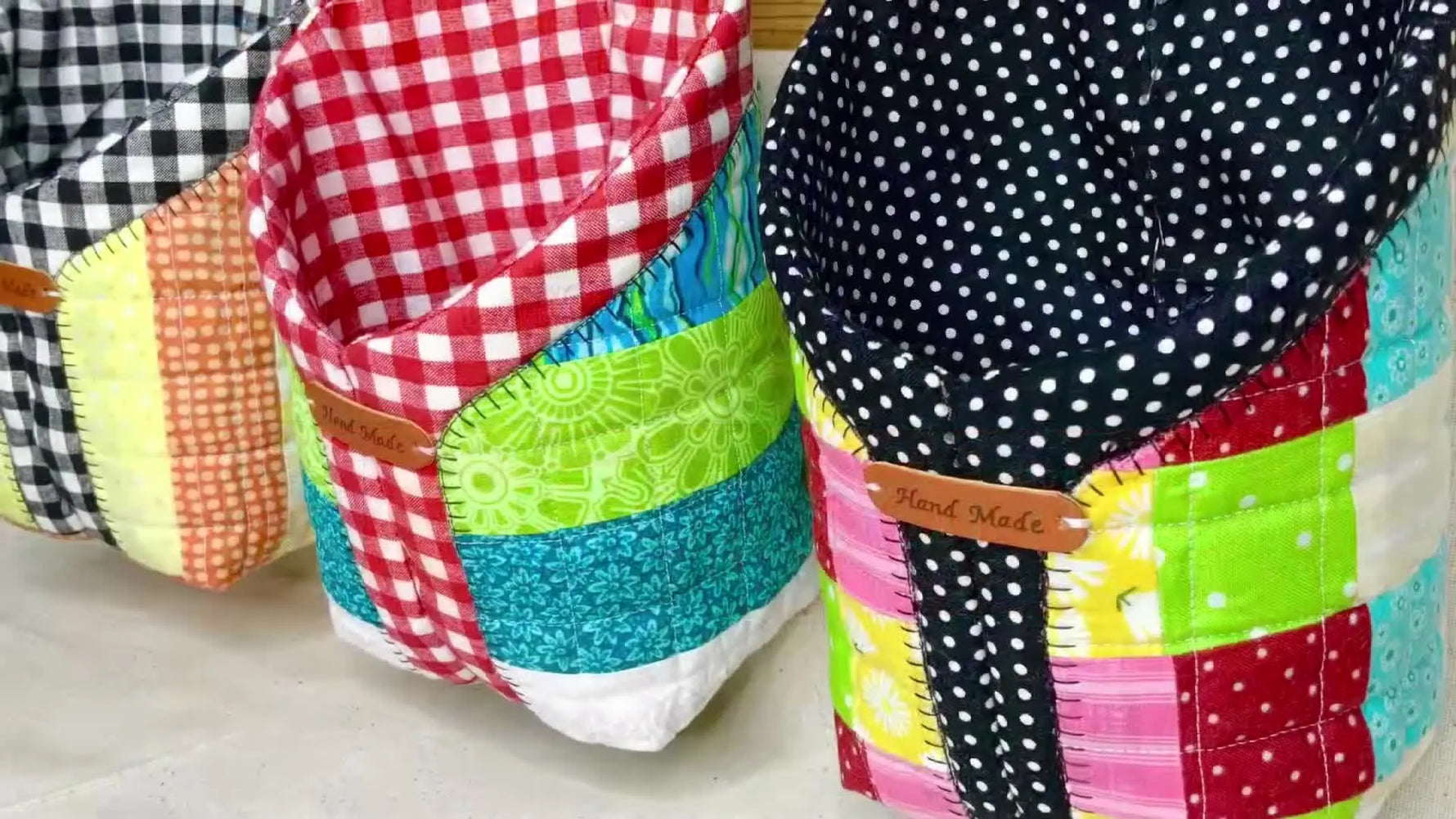 Three finished Patchy Pocket organizers hang on a wooden wall, showing the colorful patchwork fronts and clean 3D shape.