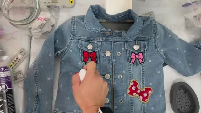 A Cricut EasyPress Mini is being used directly on an embroidered patch placed on a denim jacket to bond the adhesive evenly.