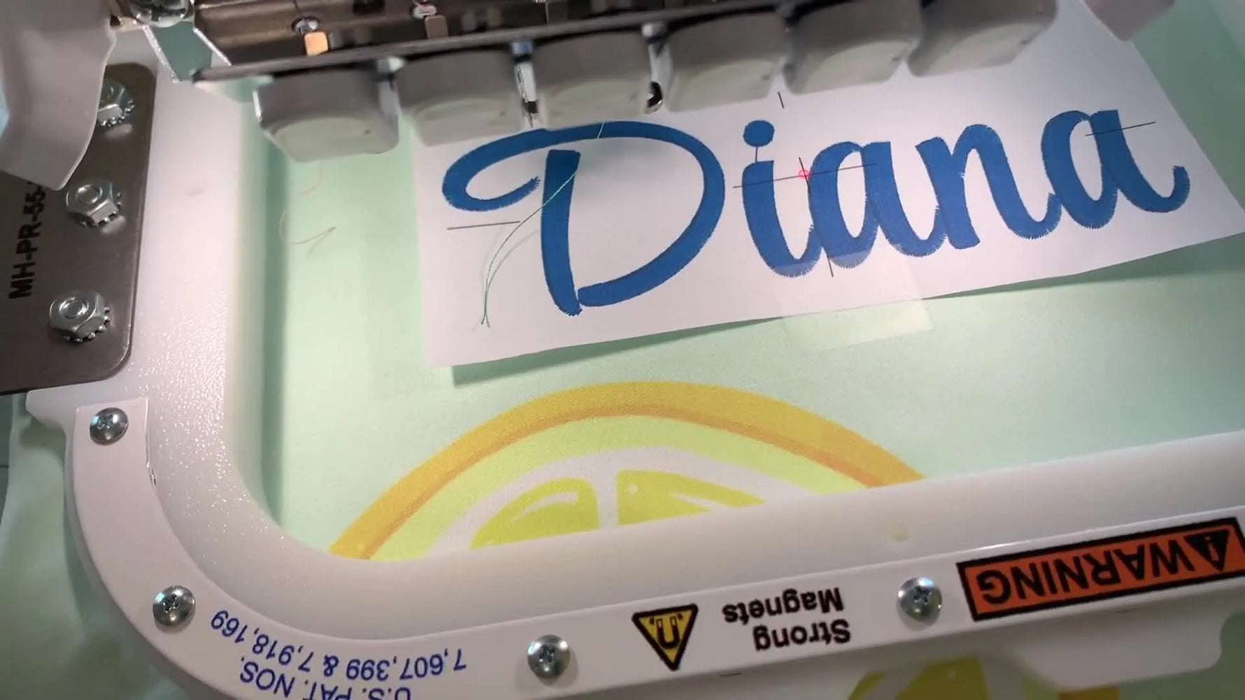 A close-up of the Brother machine’s red laser dot landing precisely on the template crosshair for perfect name placement inside a magnetic hoop.