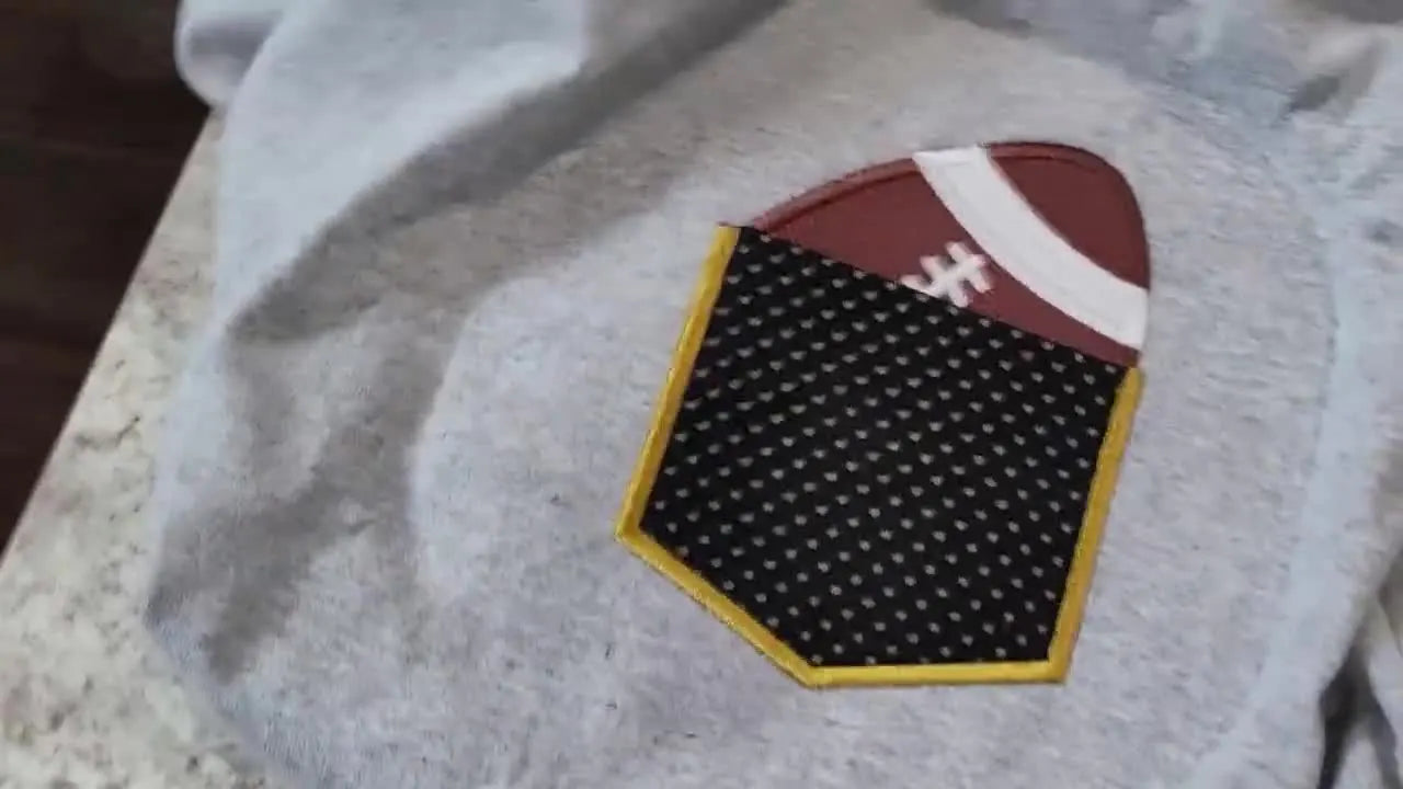 Close-up of the finished football applique pocket on a sport grey T-shirt, showing a clean satin border and a pocket opening that remains functional.