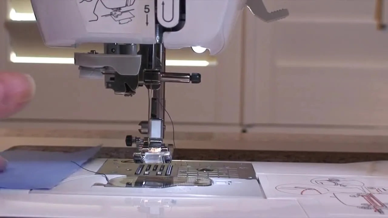 A square of blue fabric is placed over the Brother NV950 throat plate to prevent a loose needle from dropping into the bobbin area during removal.