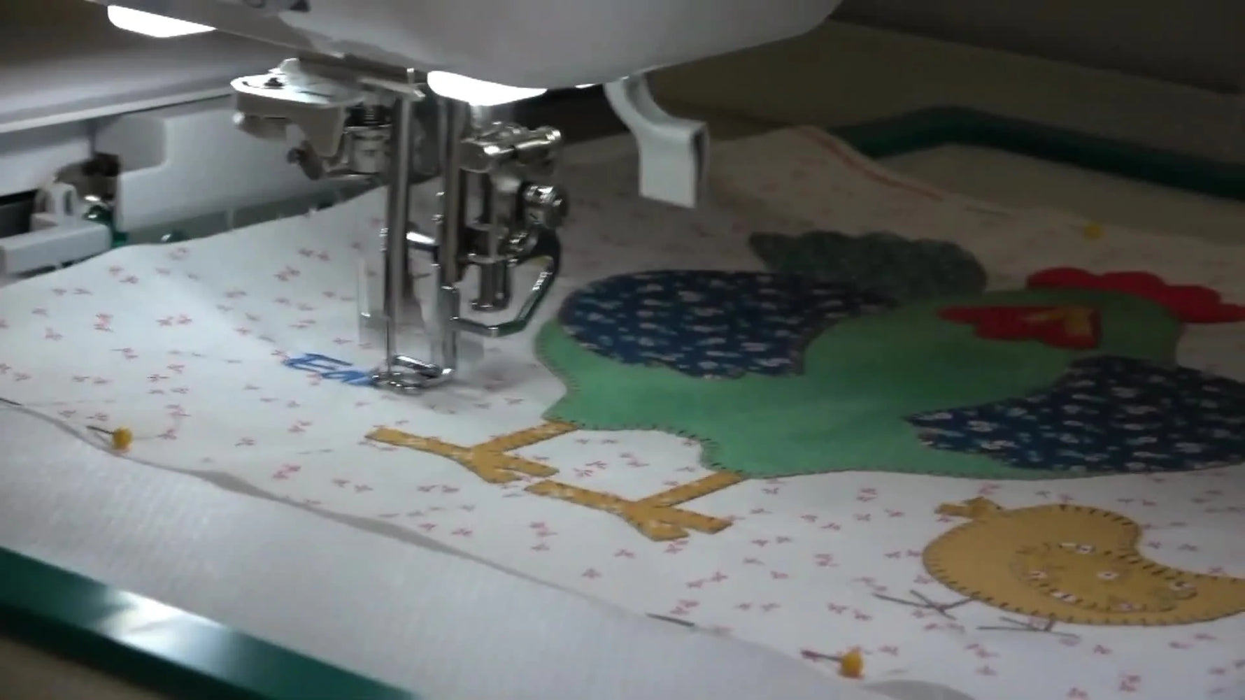A finished Edna chicken appliqué block is held up in the hoop, showing clean blanket stitching and crisp placement.