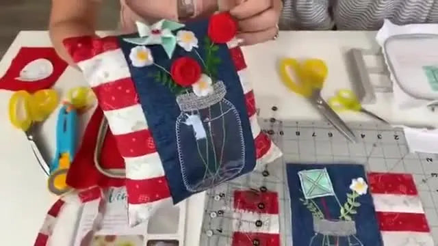 A close-up of the finished July Bench Buddy pillow showing the vinyl mason jar effect and the completed 3D pinwheel, daisies, and rosebuds.