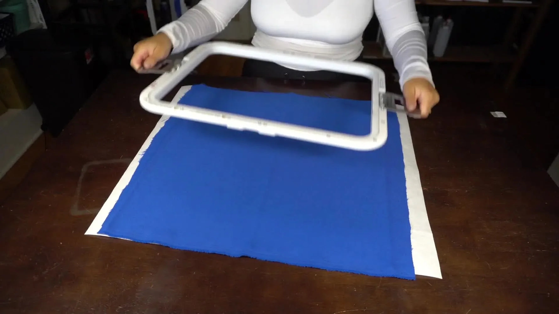 A high-angle action shot capturing the top magnetic frame snapping onto the bottom ring over fabric, showing the speed and simplicity of magnetic hooping.