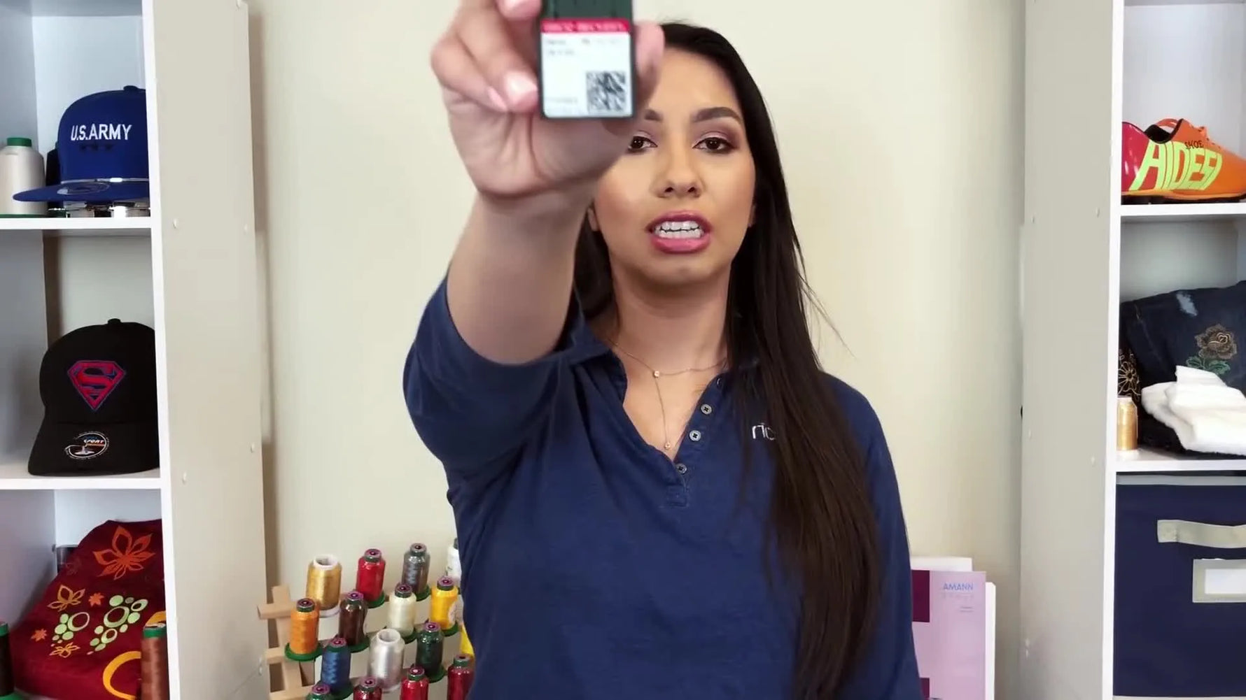 A close-up of the host holding a 75/11 embroidery needle box toward the camera to clearly identify the standard DBxK5 needle size.