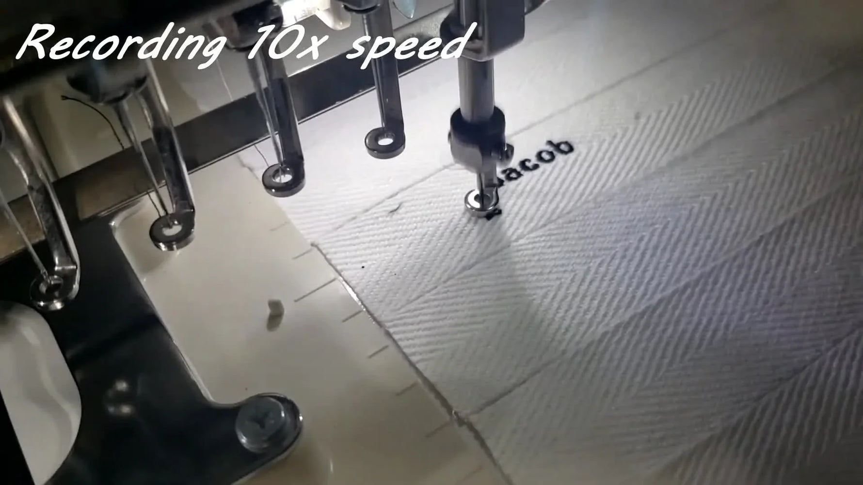 A close-up of the Janome MB-7 stitching black name text onto a sheet of 1-inch white ribbon floated on sticky stabilizer.