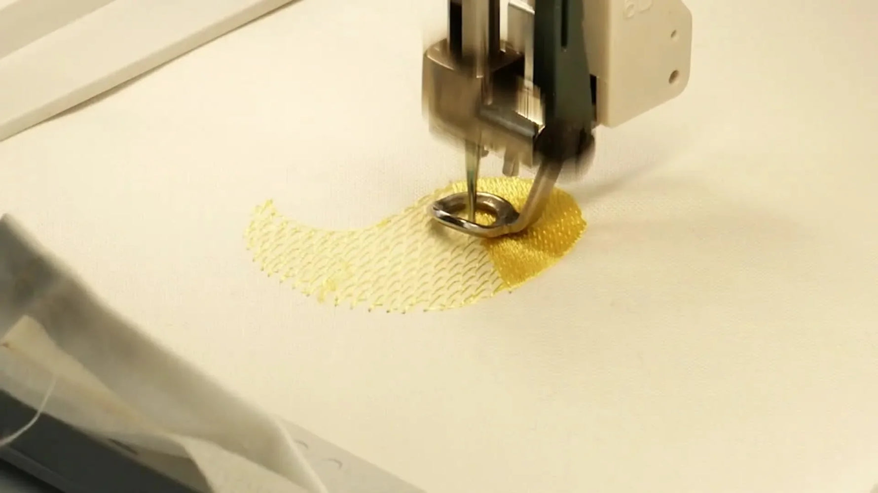 A close-up macro view of yellow rayon stitches filling the Easter chick design as the Pfaff Creative Icon 2 embroiders on a hooped white napkin.