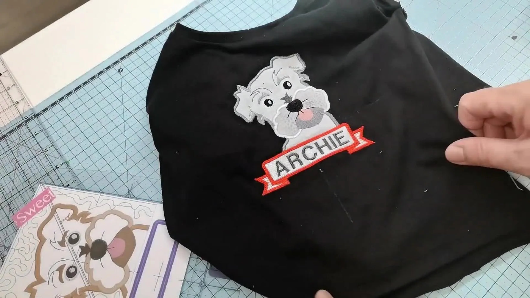 A finished child’s black T‑shirt featuring a combined embroidery of a dog, a banner, and the name “ARCHIE.”