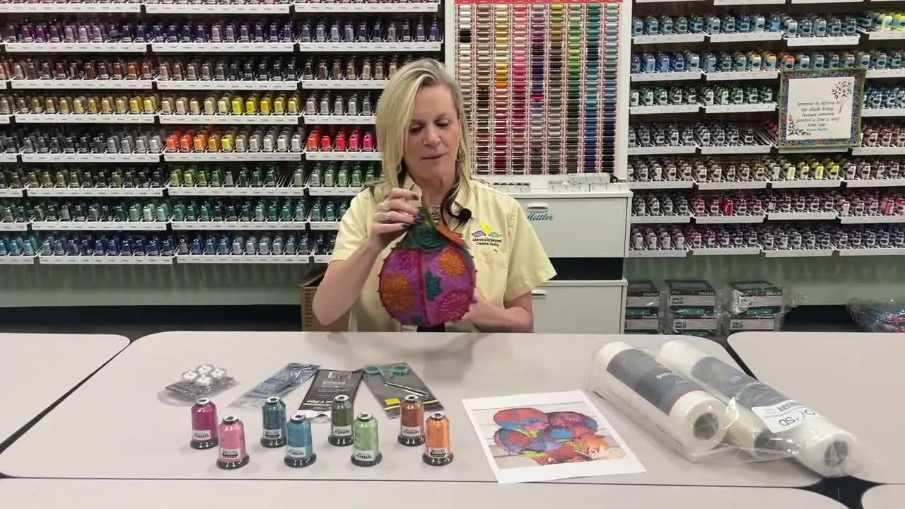 The instructor holds a finished OESD freestanding lace fall floral pumpkin, showing its 3D shape and stitched lace panels.