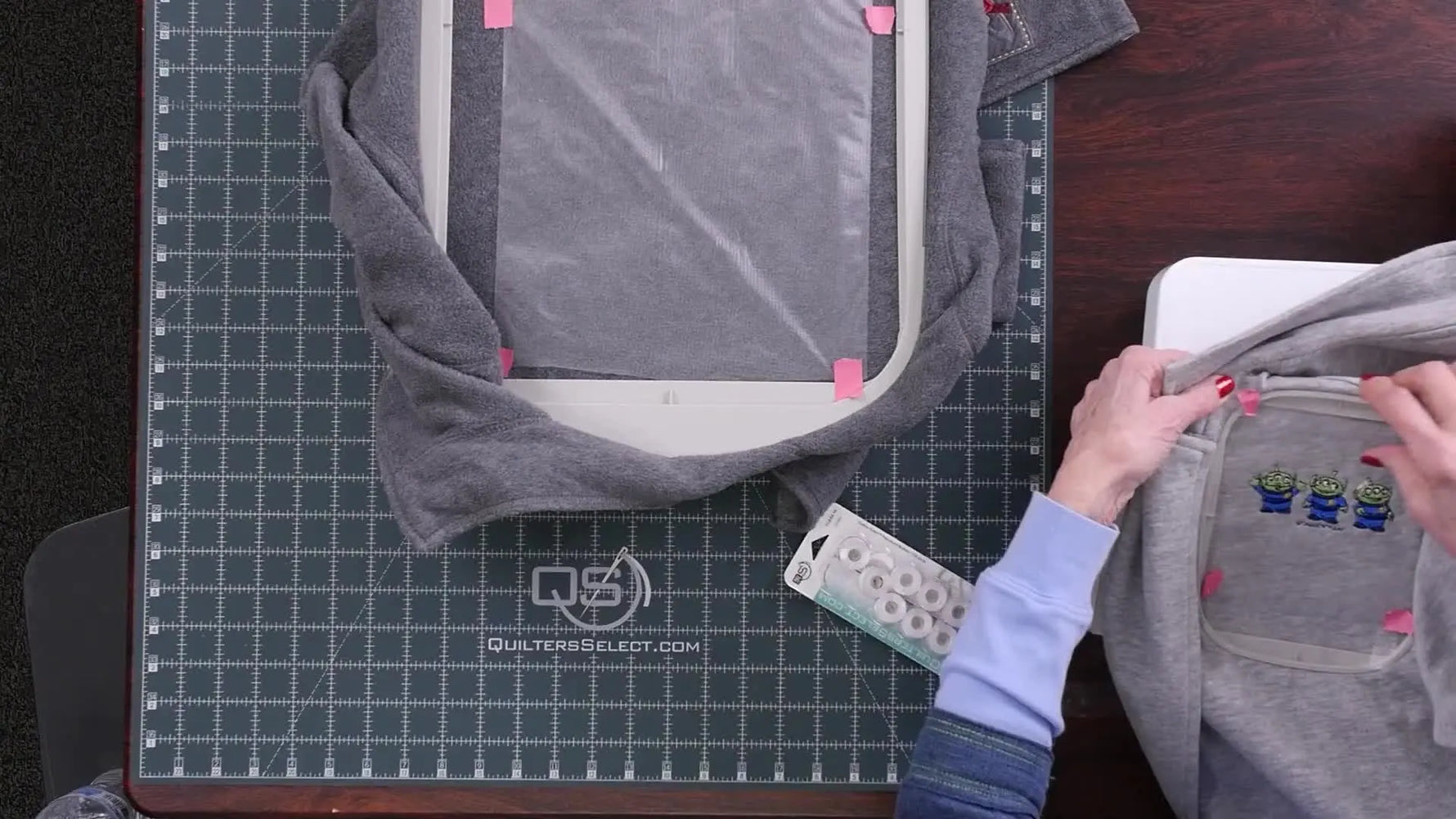 Linda holds up the finished gray lightweight knit jacket showing the three Toy Story aliens stitched cleanly with no puckering.