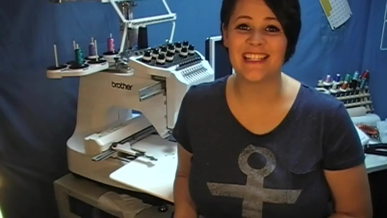 The host holds a finished, colored Peacock Doodle-It pillow that shows the crisp black outline stitches designed for kids to color in.