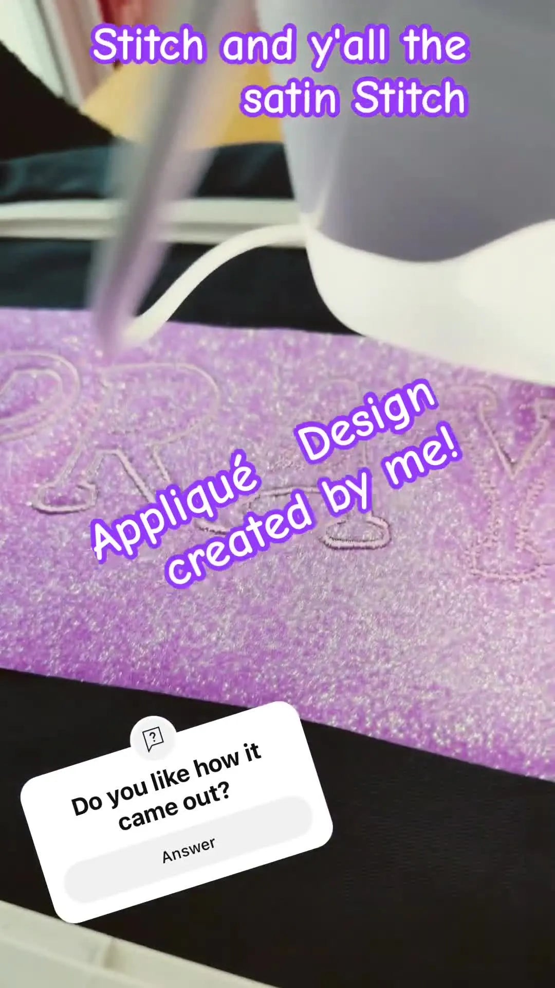 A top-down view of the finished satin-stitched word “PRAY” in purple glitter vinyl appliqué on a black garment, right before the excess vinyl is torn away.