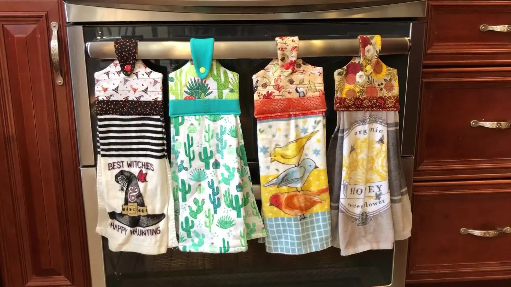 Four finished in-the-hoop towel toppers hang neatly on an oven handle, showing different seasonal themes and closures.