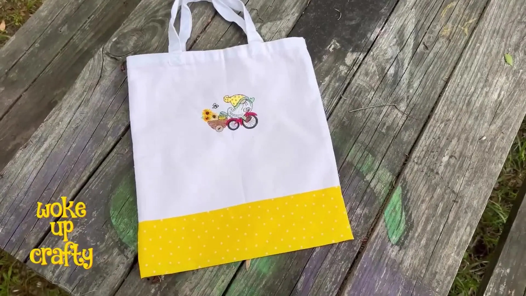 A finished white canvas market bag featuring a stitched gnome-on-a-bicycle design and a yellow polka-dot accent with matching drop-in lining.