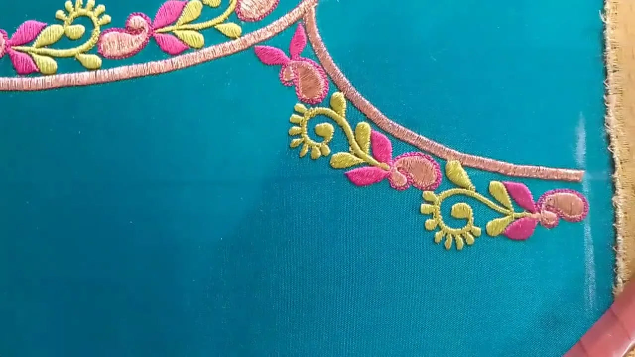 Close-up of the finished U-shaped neckline embroidery showing copper outline, magenta buds, and chartreuse vines on teal silk.
