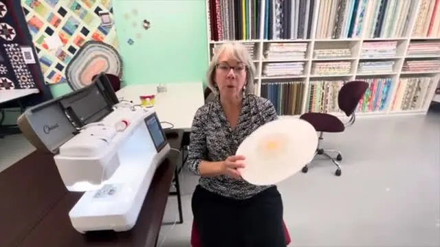 A finished rope coil placemat with a stitched mandala-style embroidery design held up in front of the machine.