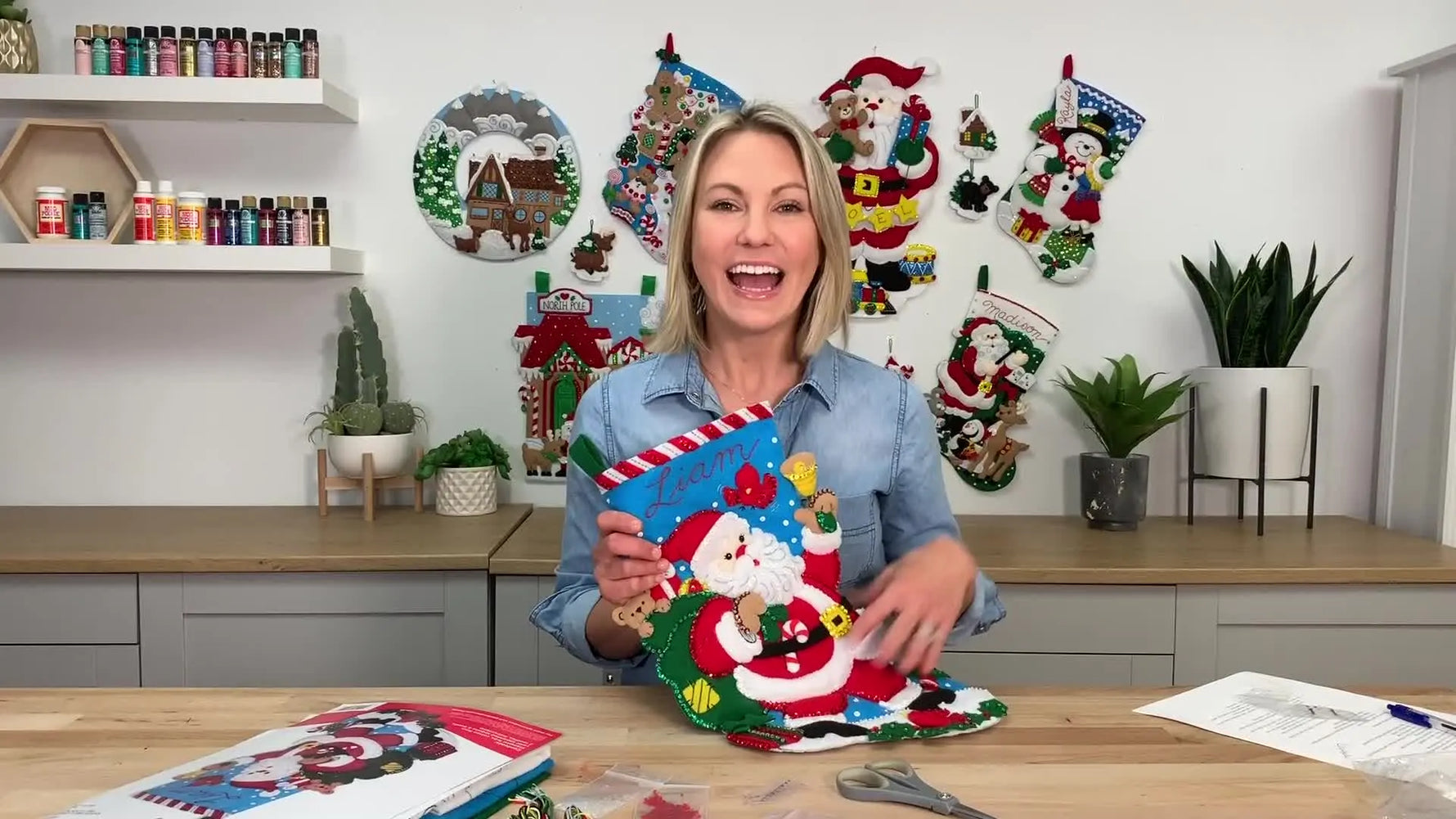 Woman smiling, holding a completed Bucilla felt stocking with a Santa design.