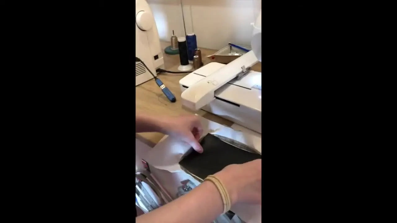 A close-up of black marine vinyl being floated over the stitched dyeline inside a 4x4 hoop under the presser foot.