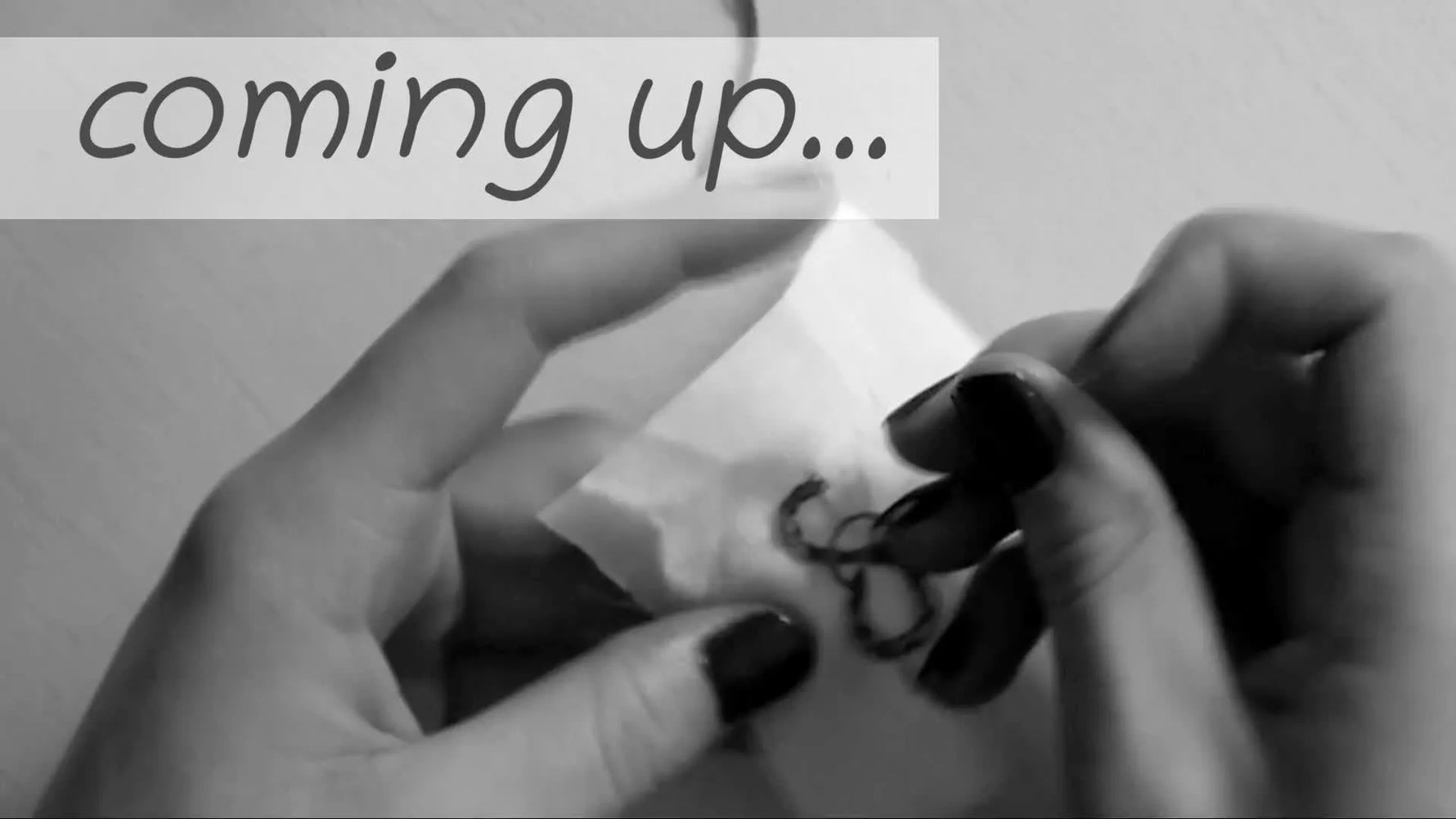 Close-up of hands embroidering the letter 'S' with pink thread on white fabric.