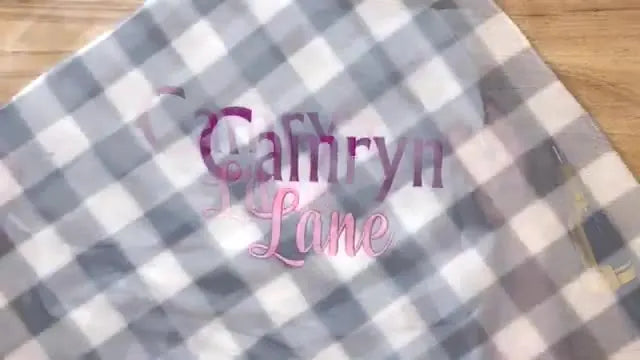 The finished ‘Camryn Lane’ name embroidery stitched in pink on a grey-and-white fleece baby blanket.
